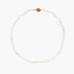 Three layered white beaded bracelets with carved orange agate lotus centerpiece and freshwater pearls on cream background.