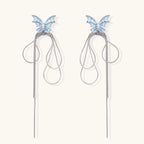 Long silver-tone earrings with powder blue enamel butterfly studs and flowing chain tassels on cream background