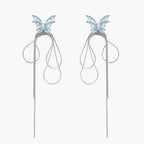 Long silver-tone earrings with powder blue enamel butterfly studs and flowing chain tassels on cream background
