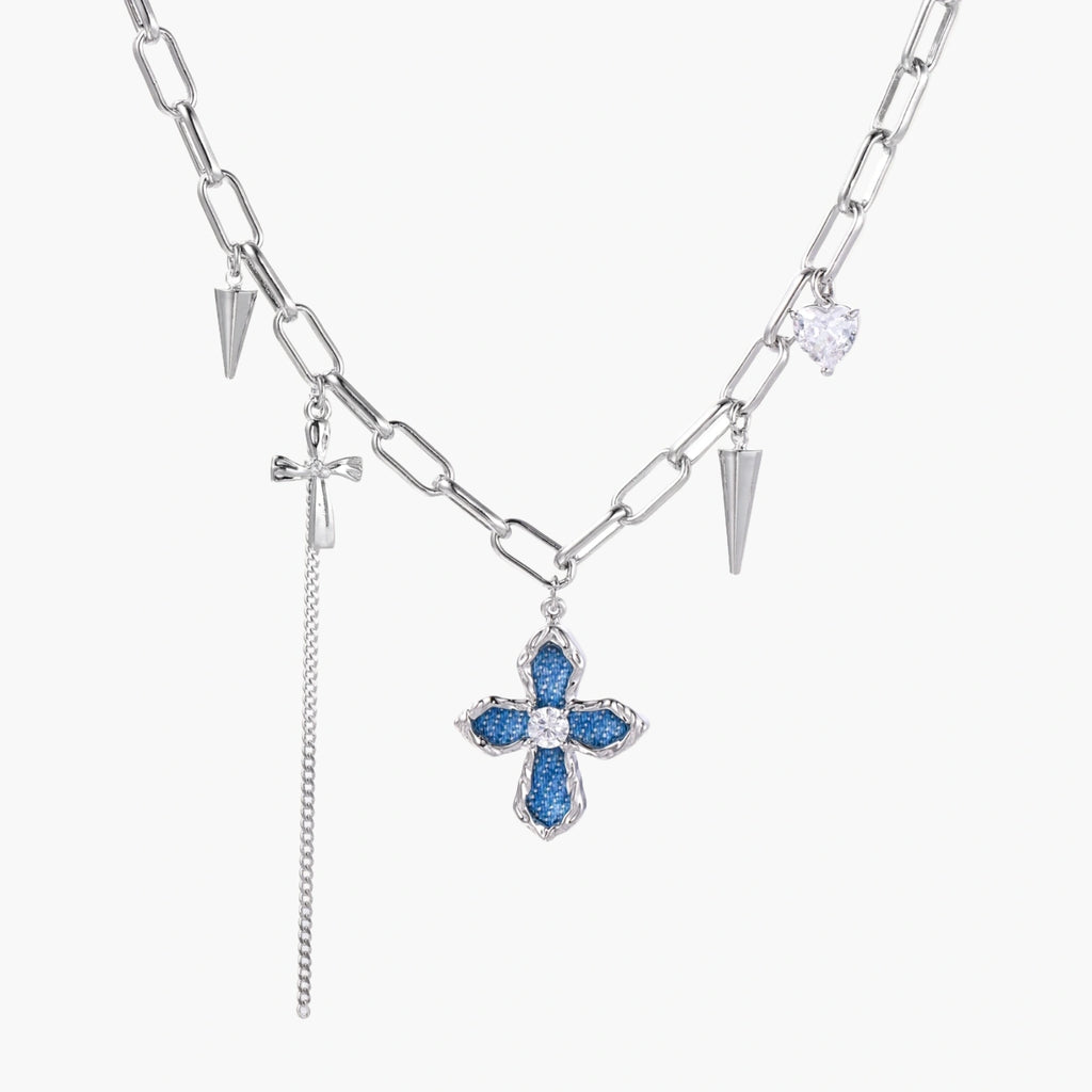 White gold plated chain necklace with blue textured cross pendant, spike charms, and mini cross detail on beige background