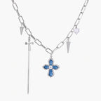White gold plated chain necklace with blue textured cross pendant, spike charms, and mini cross detail on beige background
