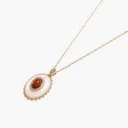 Gold pendant with oval mother-of-pearl frame, amber stone center, and crystal halo on delicate chain