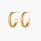 Chunky tubular hoop earrings in warm 14K gold-plated finish with smooth polished surface on cream background.