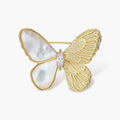 Gold-plated butterfly brooch with mother-of-pearl left wings, engraved gold right wings, and central zirconia crystal on cream background.